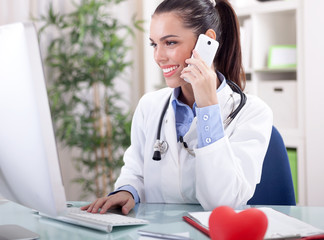 Smiling female medical doctor with telephone and computer workin