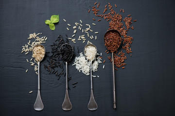 Raw rice kernels of different types over black wooden background