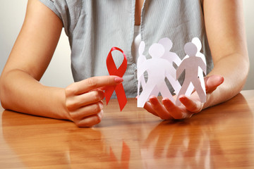 Female hands holding paper people and a red hiv ribbon, closeup
