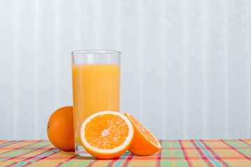 Orange fresh juice beside delicious ripe oranges on the table