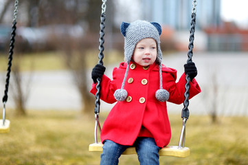 Adorable girl having fun on a swing on winter day
