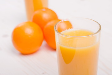 Orange fresh juice beside delicious ripe oranges on the table