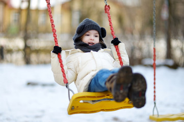 Adorable girl having fun on a swing on winter day