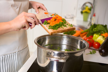 Cutting vegetables on the wooden  board are falling in the pot