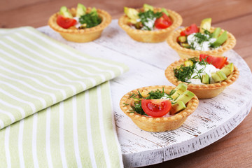 Tartlets with greens and vegetables with sauce on tray on table