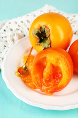 Ripe persimmons on plate, on wooden background