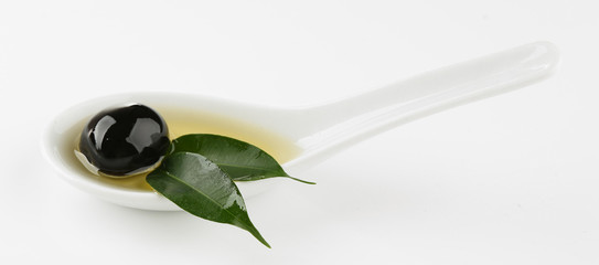 Sauce spoon with oil and black olives with leaves isolated