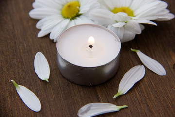 Fototapeta na wymiar Candle and daisies on wooden table seen up close