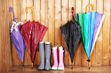 Bright umbrellas leaning against a wooden wall and gumboots