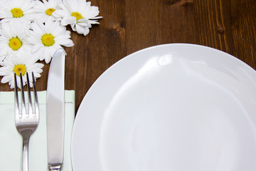 Cutlery and plate with flowers on wooden table seen up close