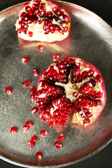 Juicy ripe pomegranate on metal plate, on dark background