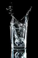 Water splash with ice in glass isolated on black