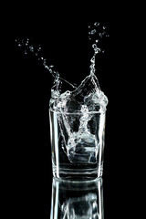 Water splash with ice in glass isolated on black