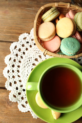 Colorful macaroons with cup of tea on wooden background