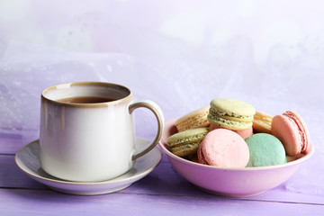 Cup of tea with colorful macaroons on color wooden background
