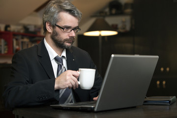 Business Man At Home Using A Laptop Computer And Drinking Coffee