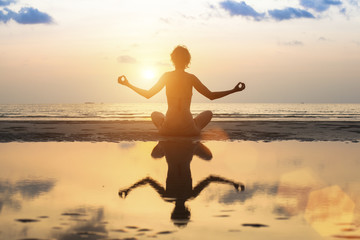 Young woman practicing yoga on the beach at amazing sunset.