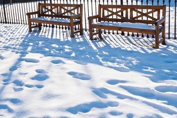 abandoned wooden benches in snowy garden with footprints