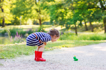 Beautiful little girl in red rain boots playing with rubber frog