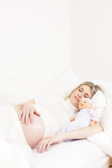 Obraz na płótnie Canvas pregnant woman sleeping in bed with a doll
