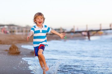 Happy little kid boy having fun with running through water in oc