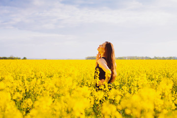 Fototapeta premium Girl touches her neck on rapeseed meadow