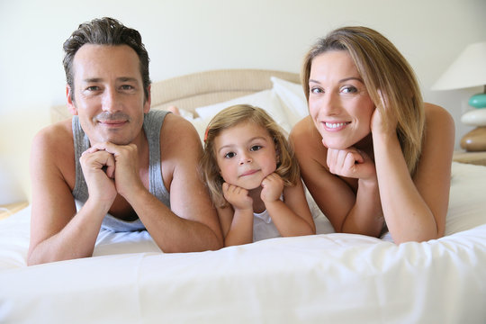 Portrait of happy family of three laying on bed