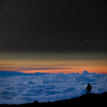 Lone climber above the clouds, looks at the starry night sky.