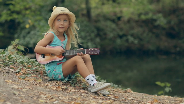 Amazing little girl with straw hat sitting by the river and