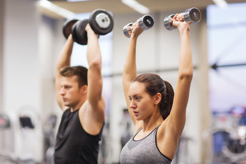 smiling man and woman with dumbbells in gym