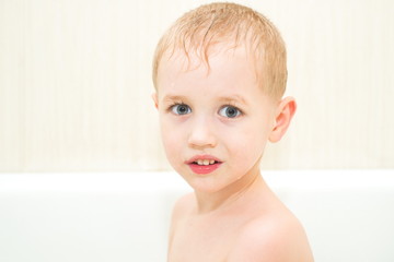Small child sitting in a bath looking at the camera and smiling