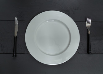 Besteck und Teller auf schwarzem Holzhintergrund