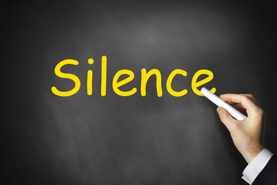 hand writing silence on black chalkboard