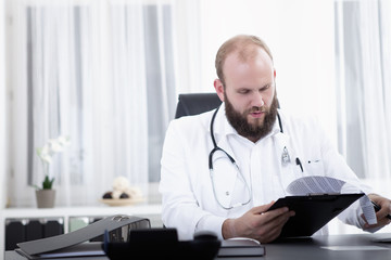 Arzt sitzt am Schreibtisch in seiner Praxis und unterschreibt