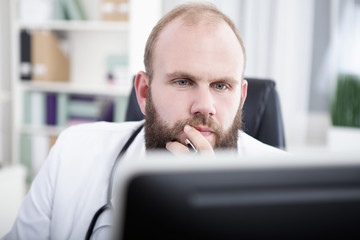 Arzt sitzt am Schreibtisch in seiner Praxis und arbeitet 
