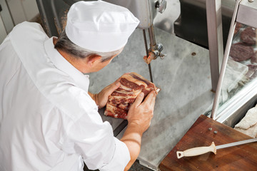 Mature Butcher Cutting Fresh Meat With Bandsaw