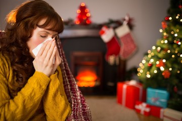 Woman sitting on sofa and blowing her nose at christmas