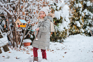happy child girl with bird feeder and seeds in winter garden