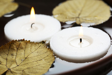 Two white candles floating with leaves on water in bowl