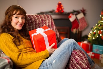 Obraz na płótnie Canvas Smiling redhead holding gift on the couch at christmas
