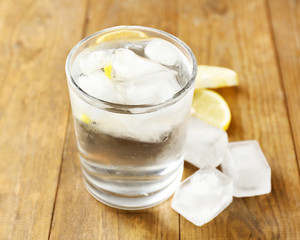 Glass of water with ice cubes on wooden table