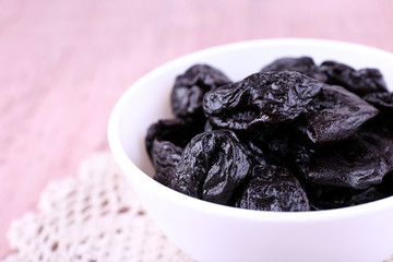 Prunes in bowl on lace doily on color wooden background