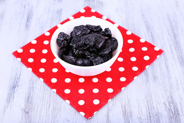 Bowl of prunes on polka-dot napkin on color wooden background