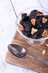 Wooden board with glass bowl of prunes and walnuts, shell and