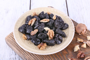 Wooden board with plate of prunes and walnuts