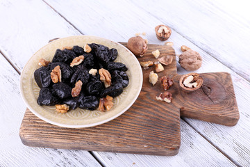 Wooden board with plate of prunes and walnuts
