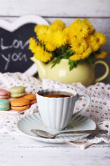 Yellow flowers in decorative teapot, cup with hot drink and