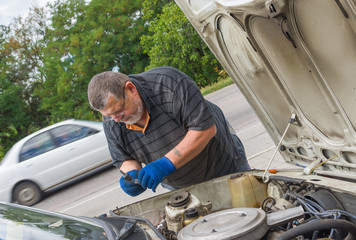 Senior man doing car repair on the road