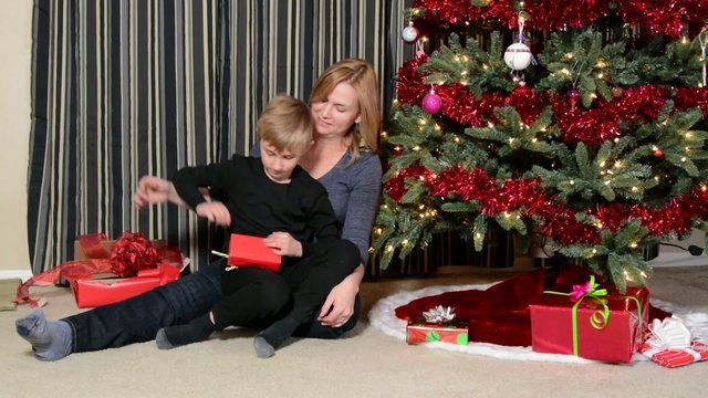 A boy opening a Christmas present with his mother