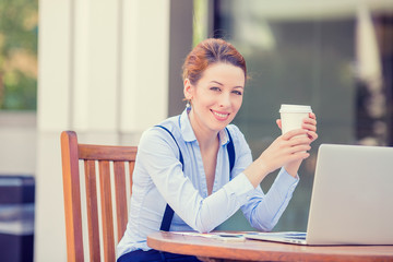 woman drinking coffee working on computer outside office